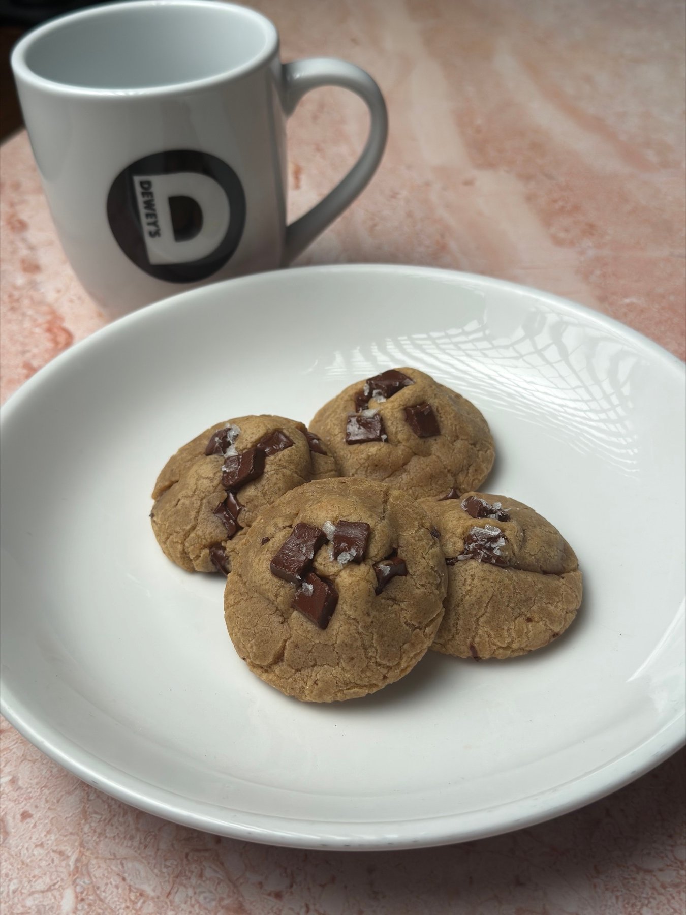 A plate of sea-salt chocolate chunk cookies beside a Dewey’s mug
